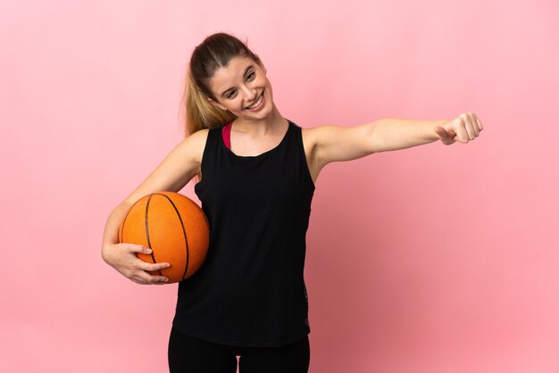 Young blonde woman playing basketball on pink background giving a thumbs up gesture