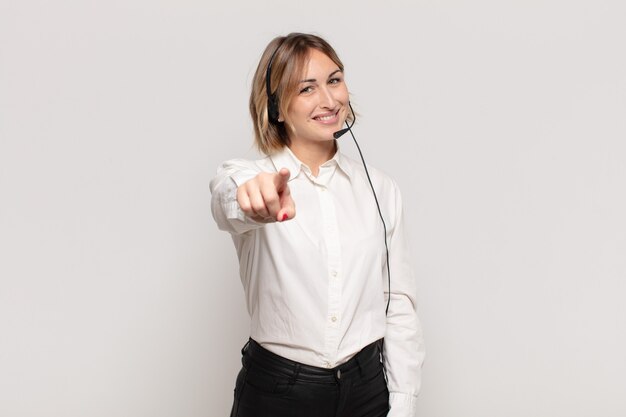 Young blonde woman pointing at camera with a satisfied, confident, friendly smile, choosing you