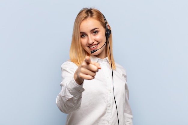 Giovane donna bionda che punta in avanti con un sorriso soddisfatto, fiducioso, amichevole, scegliendo te