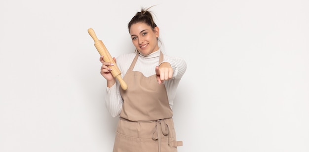 Giovane donna bionda che punta davanti con un sorriso soddisfatto, fiducioso, amichevole, scegliendo te