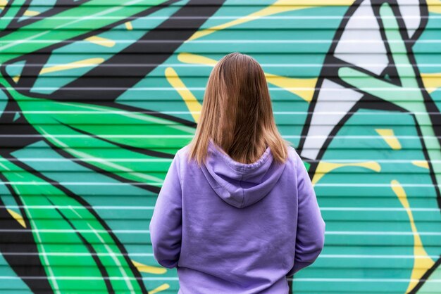 Young blonde woman in purple violet hoodie from back on green modern background copy space mockup