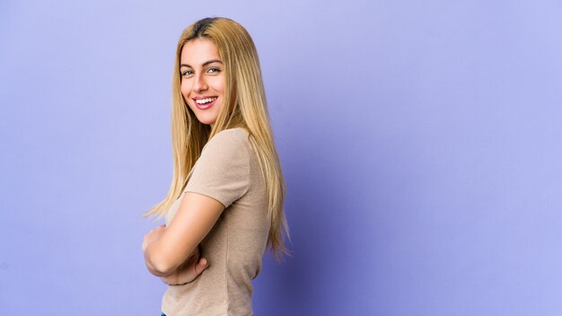 Young blonde woman on purple wall happy, smiling and cheerful.