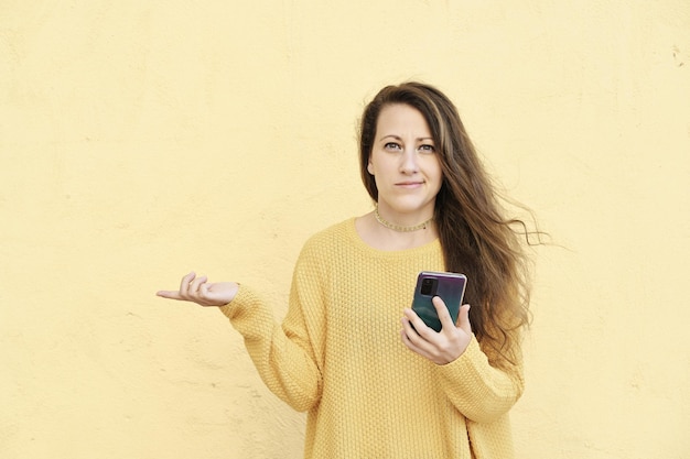 Young blonde woman puzzled and hesitating with an amused expression using a smartphone