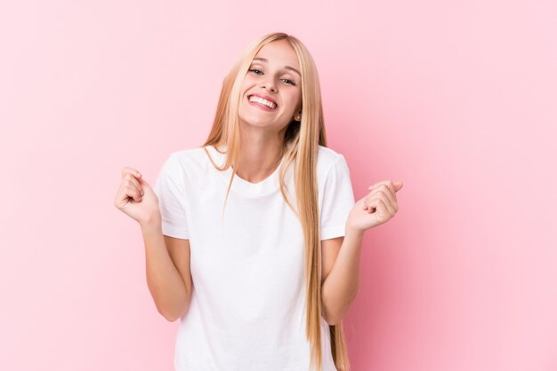 Young blonde woman raising fist, feeling happy and successful