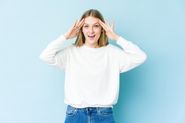 Young blonde woman receiving a pleasant surprise, excited and raising hands