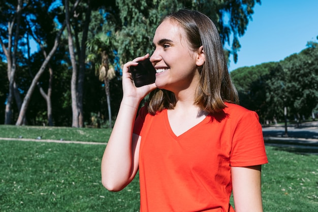 Giovane donna bionda in una camicia rossa parla al telefono cellulare in un parco