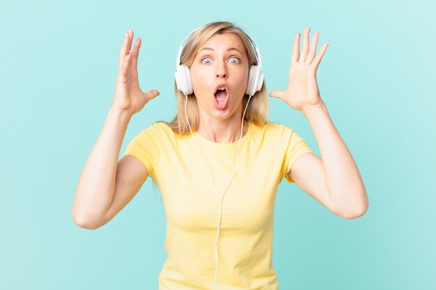 Young blonde woman screaming with hands up in the air and listening music.