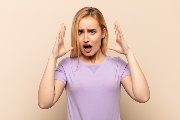 Young blonde woman screaming with hands up in the air