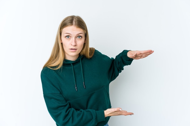 Young blonde woman shocked and amazed holding a copy space between hands.