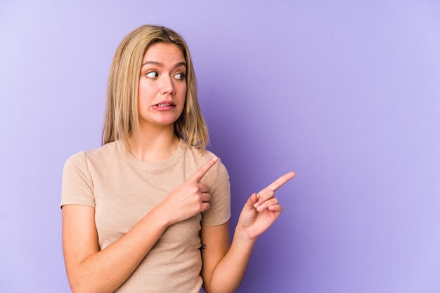 Young blonde woman shocked pointing with index fingers