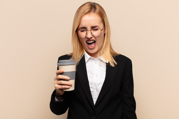 Young blonde woman shouting aggressively, looking very angry, frustrated, outraged or annoyed, screaming no