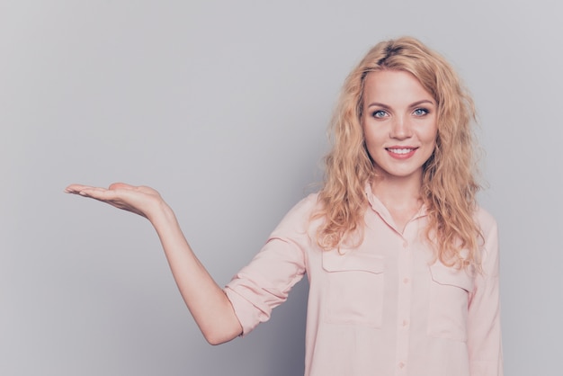 Young blonde woman showing object on palm isolated on grey