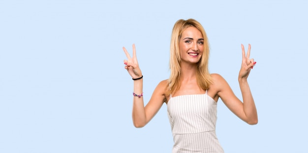 Young blonde woman showing victory sign with both hands over isolated blue 