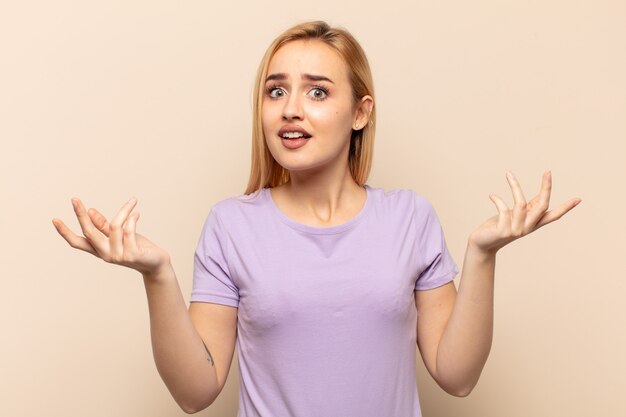 Young blonde woman shrugging with a dumb, feeling annoyed and clueless