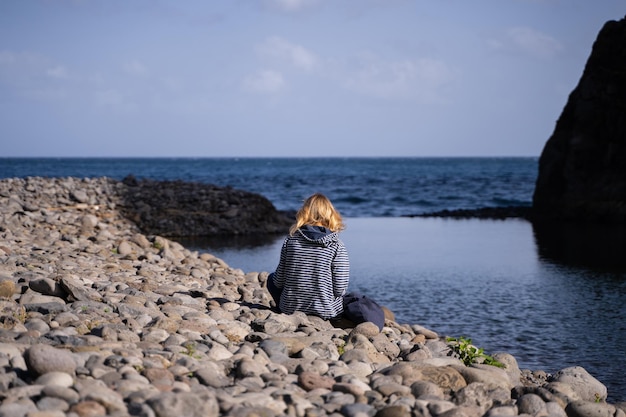 Young blonde woman sitting looking at the sea from a beach