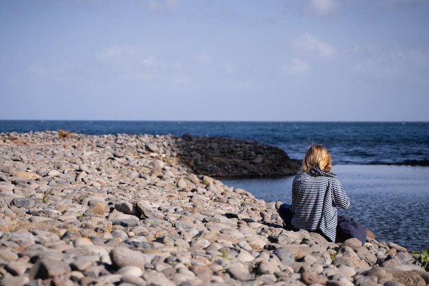 海を見ながら座っている若いブロンドの女性