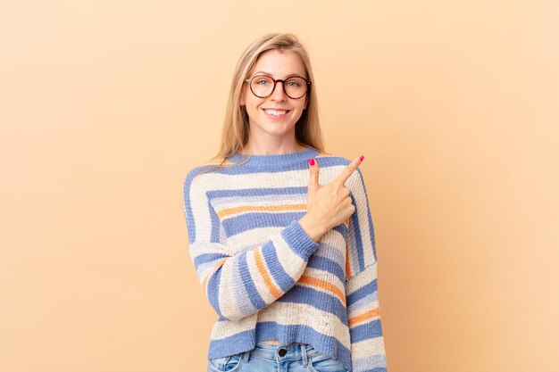 Giovane donna bionda che sorride allegramente, sentendosi felice e indicando di lato