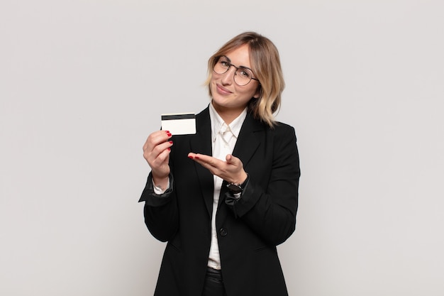 Young blonde woman smiling cheerfully, feeling happy and showing a concept in copy space with palm of hand