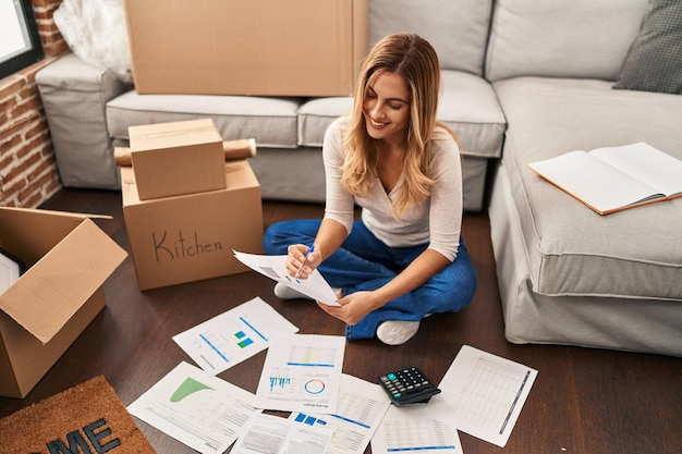 Foto giovane donna bionda che sorride sicura controllando l'economia nella nuova casa