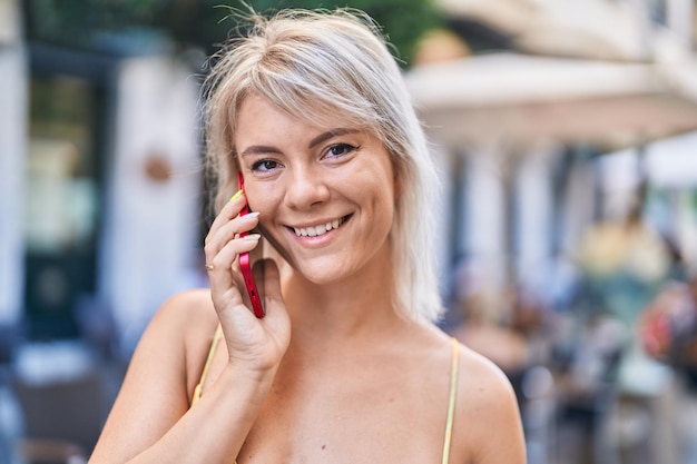 Young blonde woman smiling confident talking on the smartphone at street