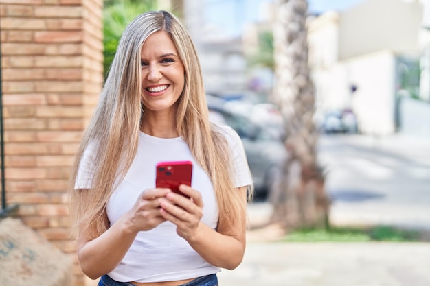거리에서 스마트폰을 사용하여 자신감 있게 웃고 있는 젊은 금발 여성