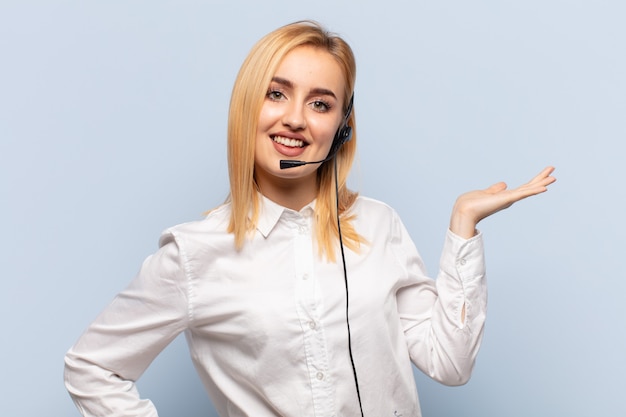 Young blonde woman smiling, feeling confident, successful and happy, showing concept or idea on copy space on the side