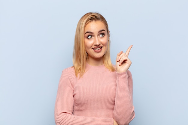 Young blonde woman smiling happily and looking sideways, wondering, thinking or having an idea