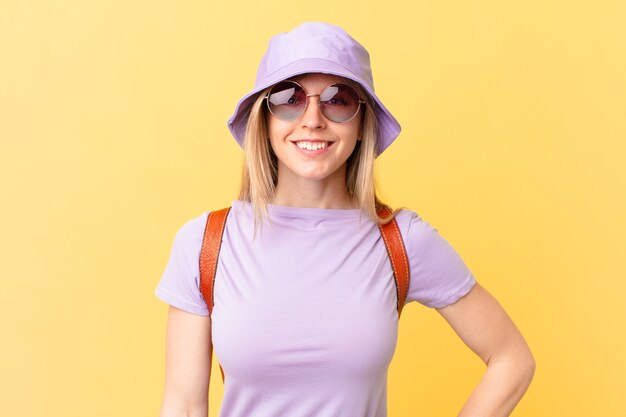 Young blonde woman smiling happily with a hand on hip and confident