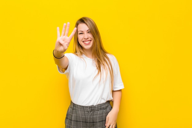 Young blonde woman smiling and looking friendly, showing number four or fourth with hand forward, counting down against orange wall