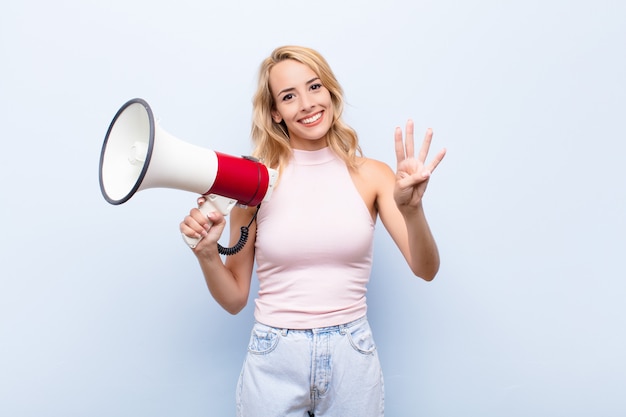 Young blonde woman smiling and looking friendly, showing number four or fourth with hand forward, counting down with a megaphone