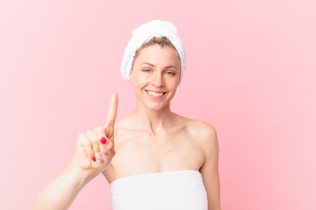 Young blonde woman smiling and looking friendly, showing number one and after shower