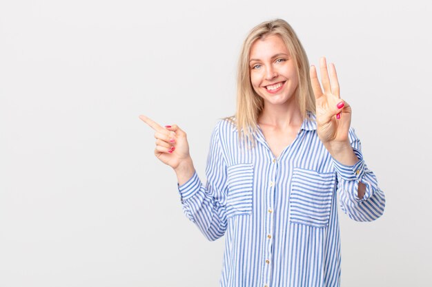 Young blonde woman smiling and looking friendly, showing number three