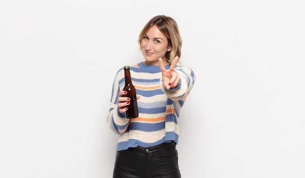 Young blonde woman smiling and looking happy, carefree and positive, gesturing victory or peace with one hand