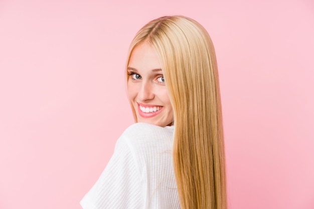 Young blonde woman smiling on a pink wall