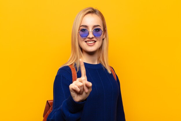 Young blonde woman smiling proudly and confidently making number one pose triumphantly, feeling like a leader