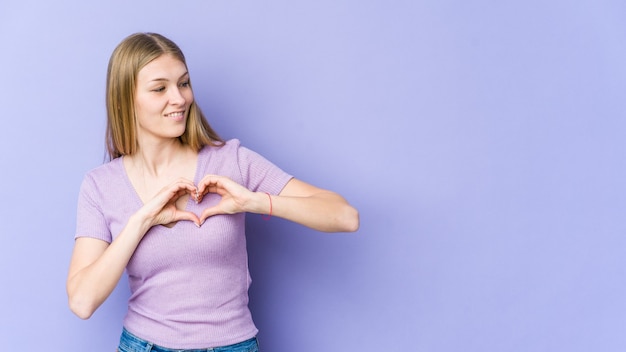 Young blonde woman smiling and showing a heart shape with hands