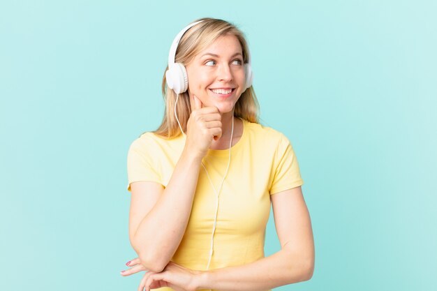 Young blonde woman smiling with a happy, confident expression with hand on chin and listening music.