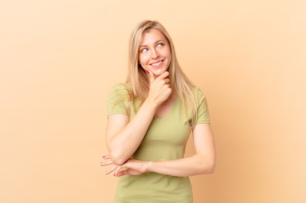 Young blonde woman smiling with a happy, confident expression with hand on chin