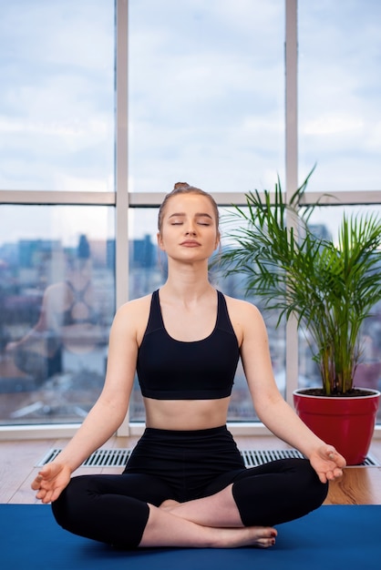 Giovane donna bionda in abiti sportivi sta meditando su una stuoia di yoga con gli occhi chiusi