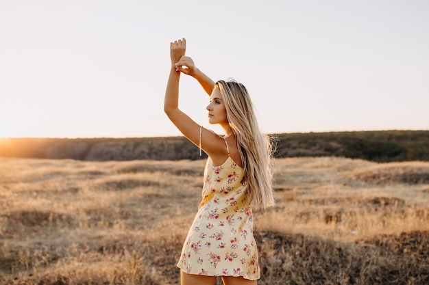 Young blonde woman standing in a field with dry grass in sunset light