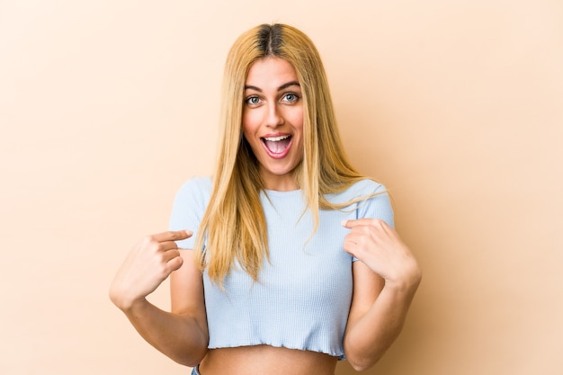 Young blonde woman surprised pointing with finger, smiling broadly