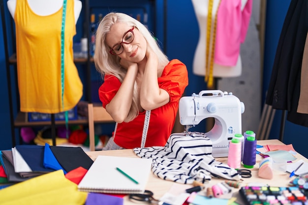 Young blonde woman tailor stressed using sewing machine at sewing studio