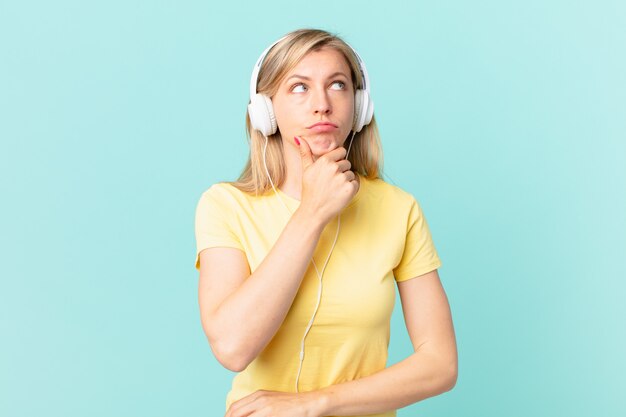 Young blonde woman thinking, feeling doubtful and confused and listening music.