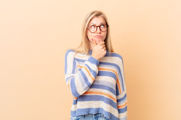 Giovane donna bionda che pensa, si sente dubbiosa e confusa