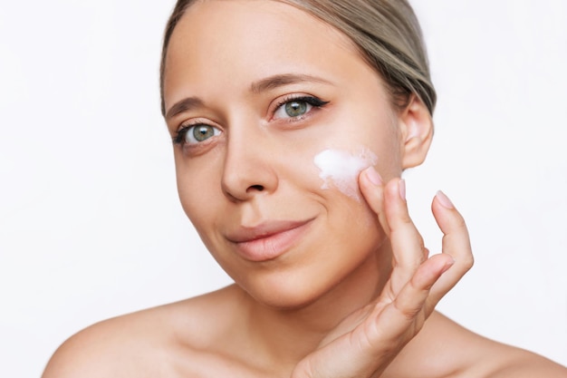 A young blonde woman touching the face with her hand applying a cream on the skin