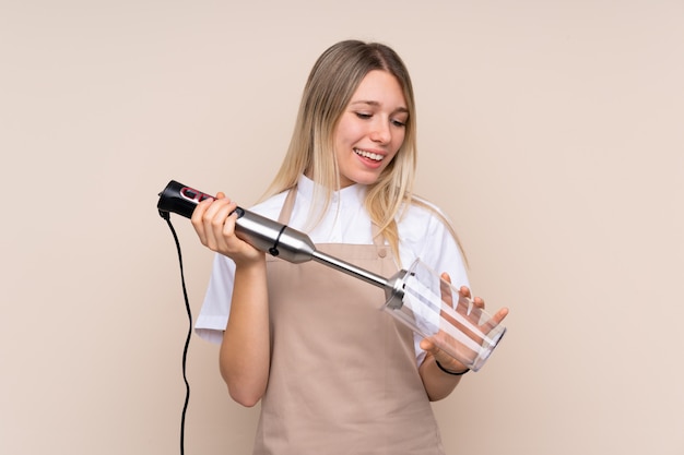 Young blonde woman using hand blender