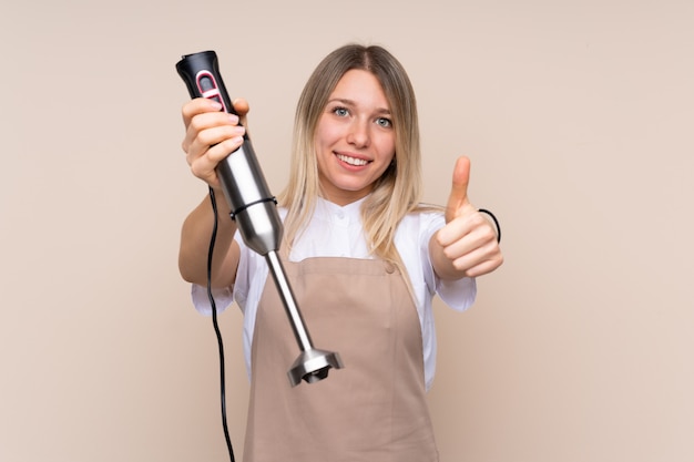 Young blonde woman using hand blender