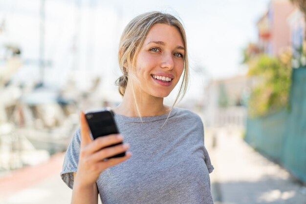 Young blonde woman using mobile phone at outdoors with happy expression