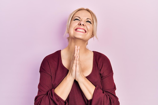 Young blonde woman wearing casual winter sweater begging and praying with hands together with hope expression on face very emotional and worried begging