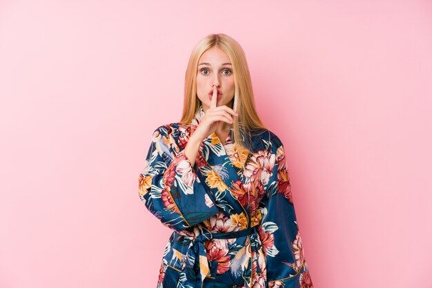 Young blonde woman wearing a kimono pajama keeping a secret or asking for silence.